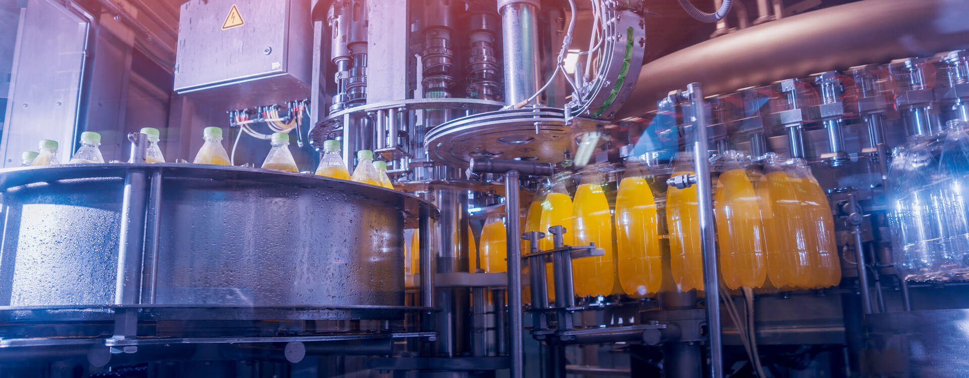 The bottles pass through a line of beverage production and filling machines and are filled with orange drinks